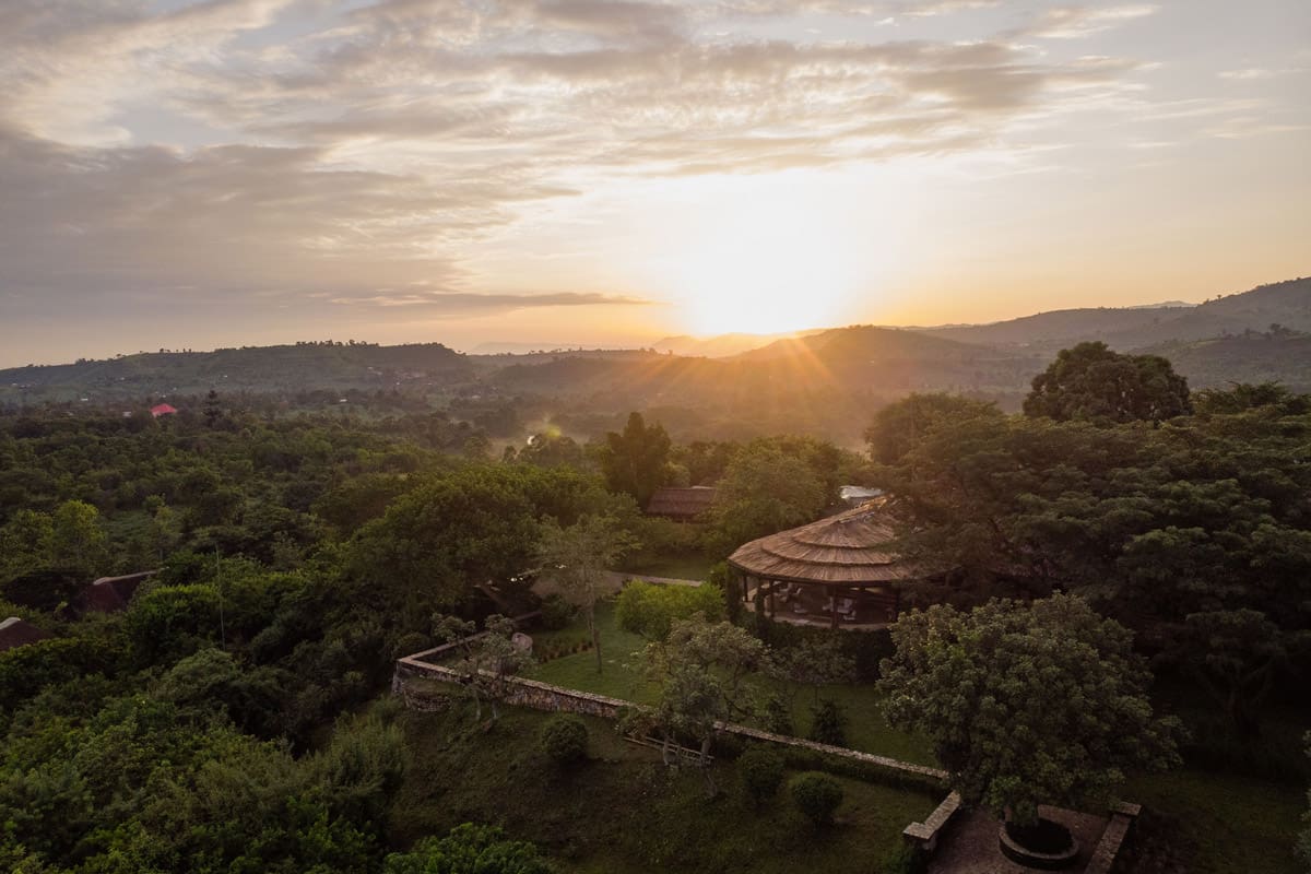 Aerial view of Kyambura Gorge Lodge at sunrise, surrounded by lush greenery and rolling hills in Uganda.